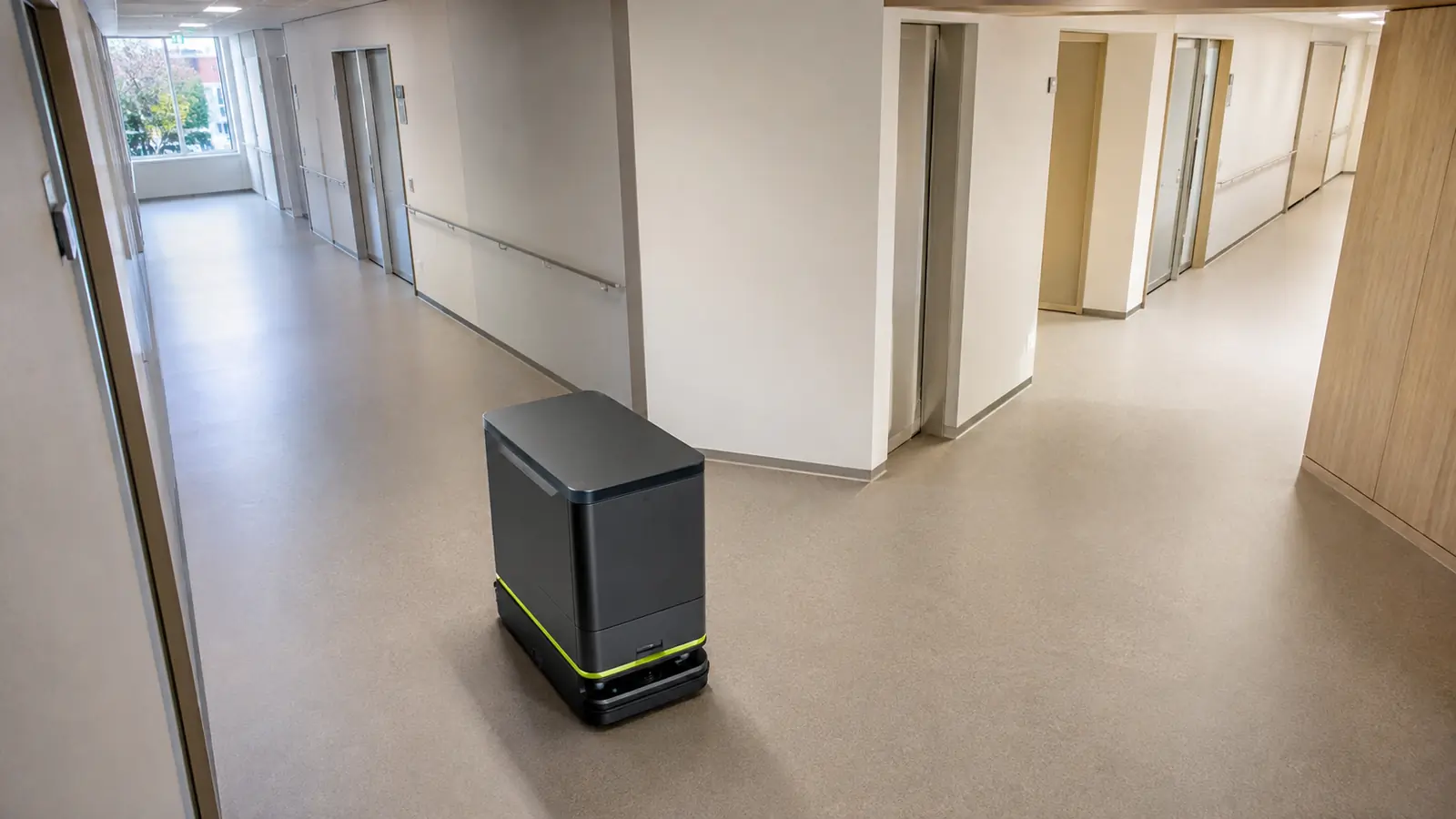 Autonomer Transportroboter navigiert selbstständig durch einen Krankenhausflur mit Aufzügen.