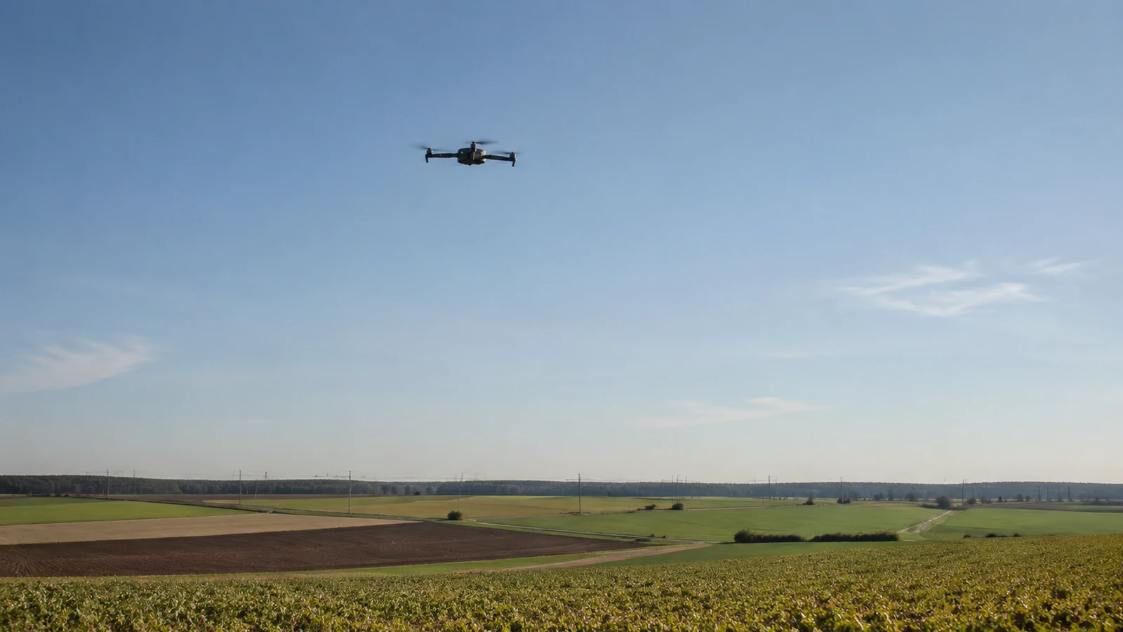 Profi-Drohne fliegt über offene Landschaft mit Infrastrukturlinie am Horizont, klare Sicht.