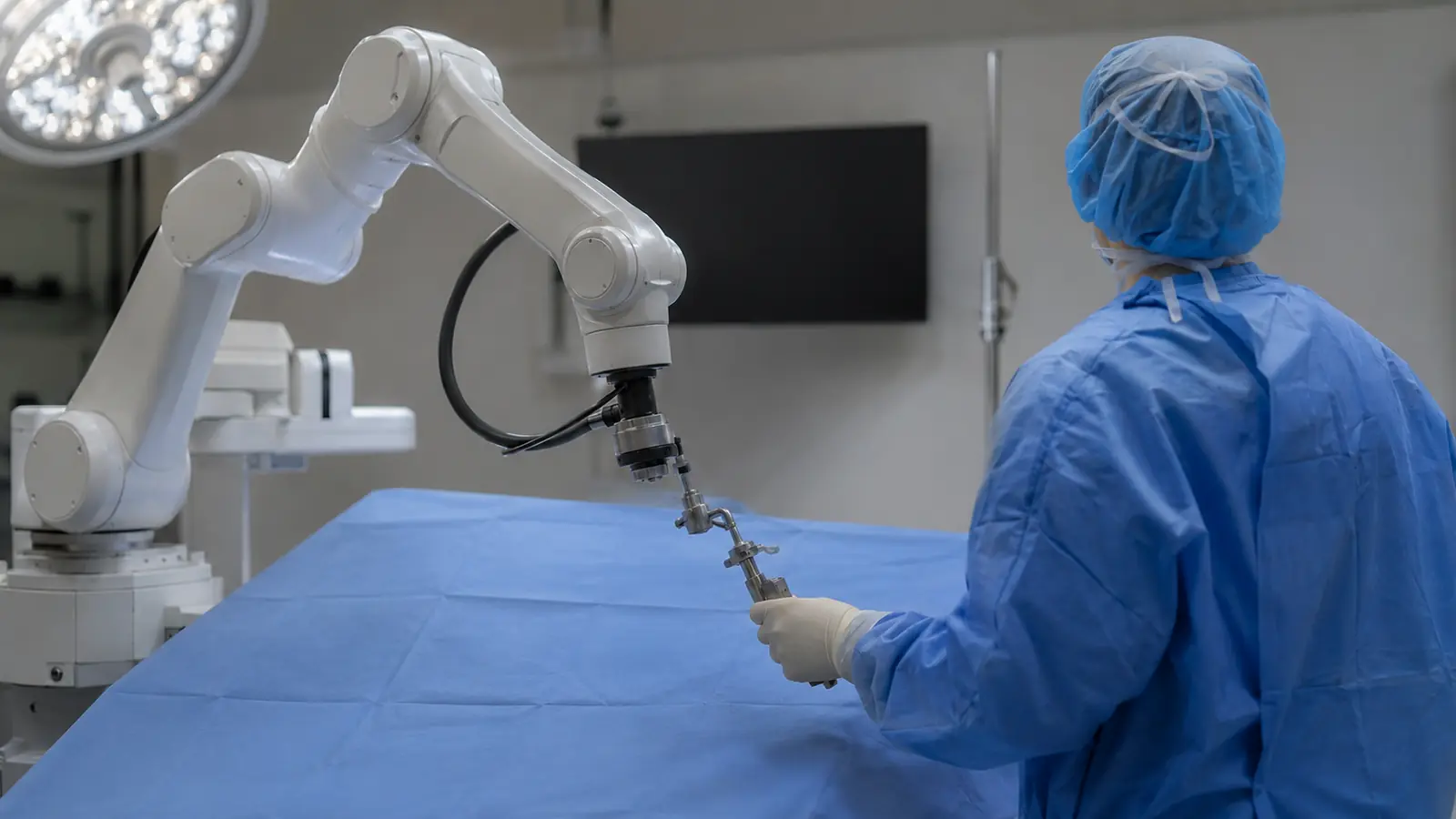 Roboterarm bei der Knie-OP ueber dem vollstaendig abgedeckten Operationsfeld, Operateur fuehrt das Werkzeug