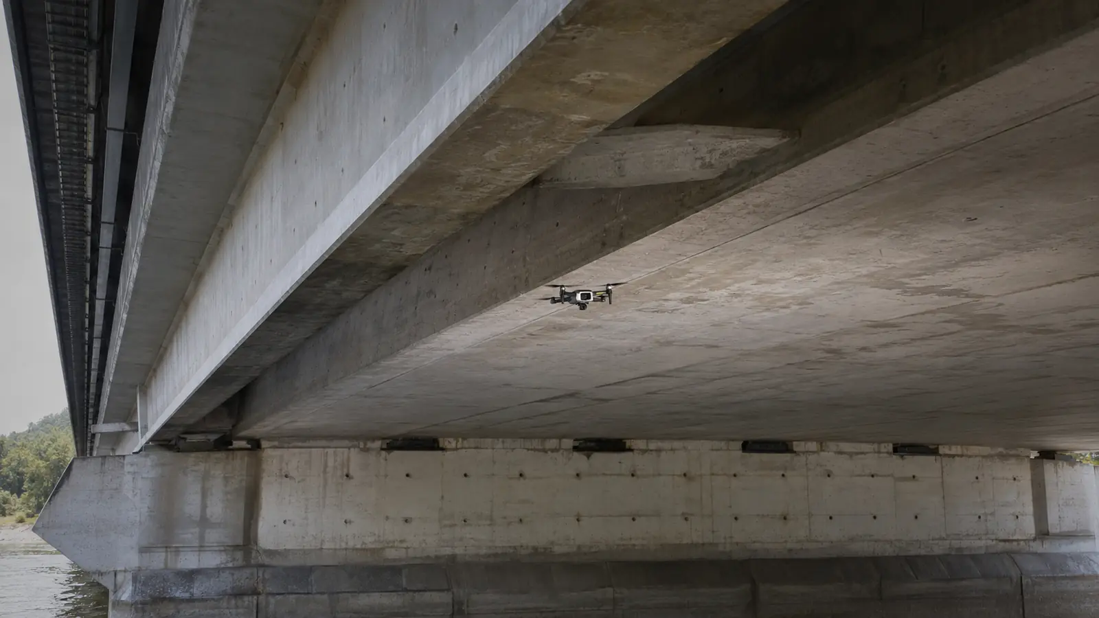 Inspektionsdrohne im Schwebeflug unter einem Brückenträger, Betonstruktur im Vordergrund.